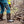 Load image into Gallery viewer, Person wearing blue jeans and black boots with a yellow vest, standing on rocky terrain and holding a shovel.