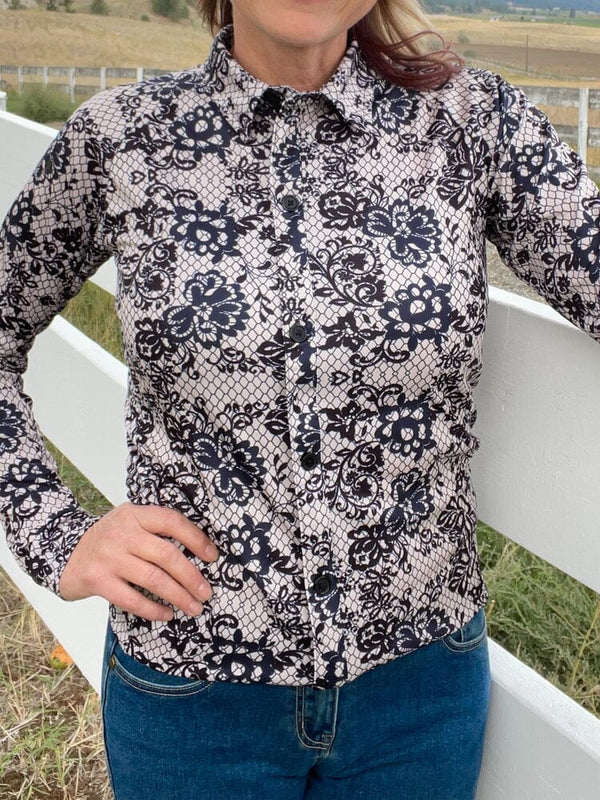 woman outside standing by white wood fence, wearing black and white lace pattern shirt and black western hat