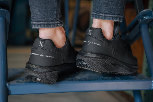 person wearing black work sneakers with white text standing on a blue metal surface.