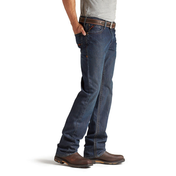 side view of man wearing grey shirt tucked into dark blue jeans wearing brown work boots