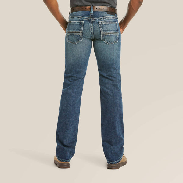 back view of person wearing distressed denim dark blue jeans with brown belt, charcoal shirt, and tan boots