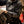Load image into Gallery viewer, man wearing charcoal colored zip up jacket with Ariat written down the sleeve in green camo while using a tool