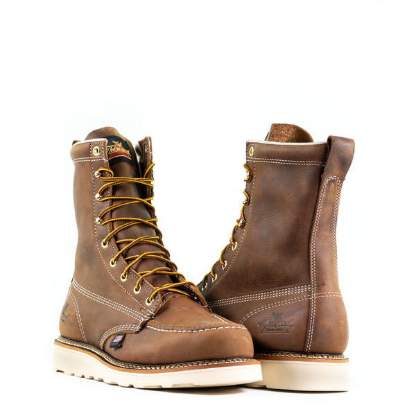 alternating pair of mens brown logger boots with white sole and stitching and yellow/brown laces. black thorogood logo stamped on heel.