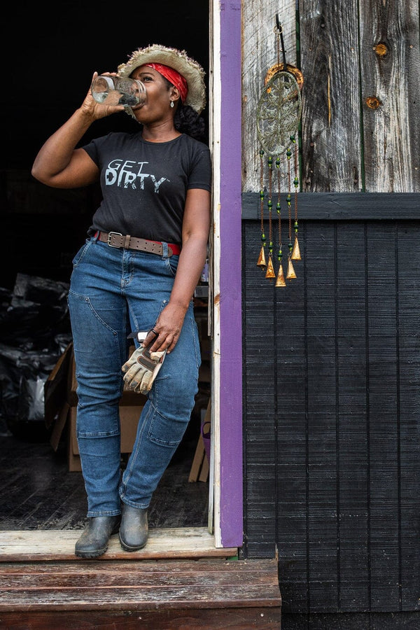  women leaning against doorframe drinking from a mason jar wearing blue jeans and a black crew neck t-shirt that says "Get Dirty"