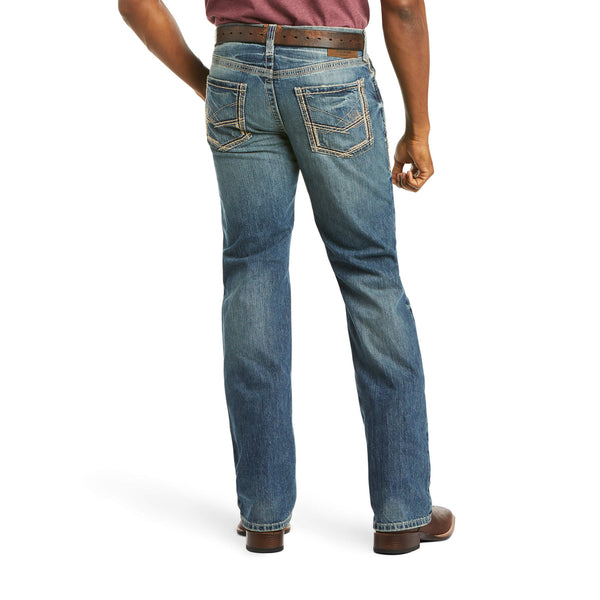 back view of person wearing medium wash denim jeans distressed with brown belt and boots