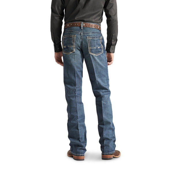 back view of Man wearing a dark grey button up tucked into faded wash blue jeans with a gold belt buckle and cowboy boots
