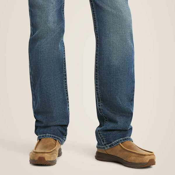 front lower legs of person wearing blue jeans and tan moccasin shoes