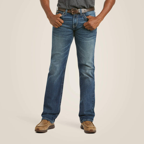 front view of person wearing distressed denim dark blue jeans with brown belt, grey shirt, and tan boots