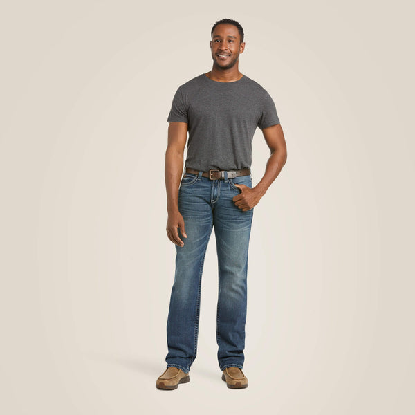 full body view of person wearing distressed denim dark blue jeans with brown belt, charcoal shirt, and tan boots