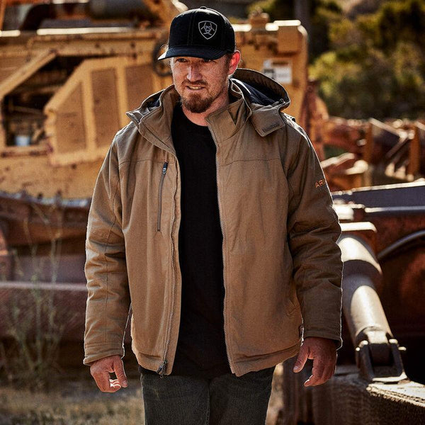 man wearing brown insulated jacked and black hat walking in front of construction equipment 