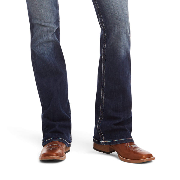 close up view of dark blue boot cut denim jeans with white stitching and medium brown square toe western boots