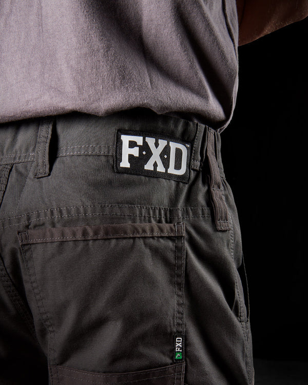 close rear view of black work pants with FXD logo tag on waistband and back pocket with grey stitching