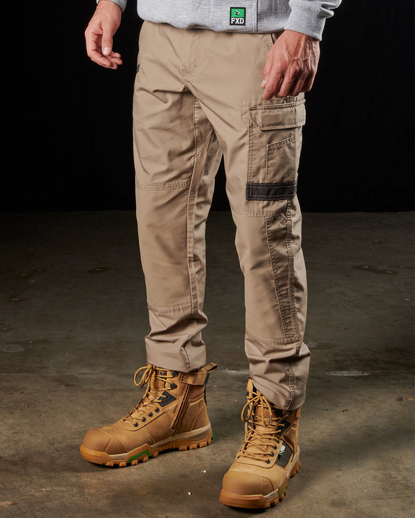 front view of man wearing khaki light weight work pants with black details on cargo pockets, light grey sweatshirt, and tan boots