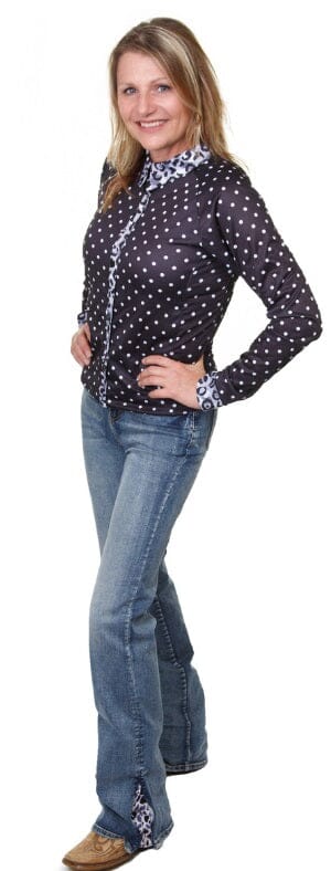 woman with hands on waist wearing black and white polka dot long sleeve shirt with leopard print collar and cuffs, light blue denim jeans and tan boots.
