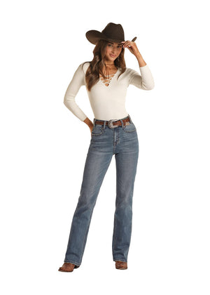 brunette woman wearing medium blue denim jeans, cream long sleeve top, and brown boots, belt, and cowgirl hat