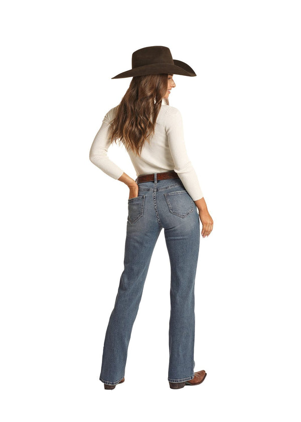 back of brunette woman wearing medium blue denim jeans with hand in back pocket, cream long sleeve top, and brown boots, belt, and cowgirl hat