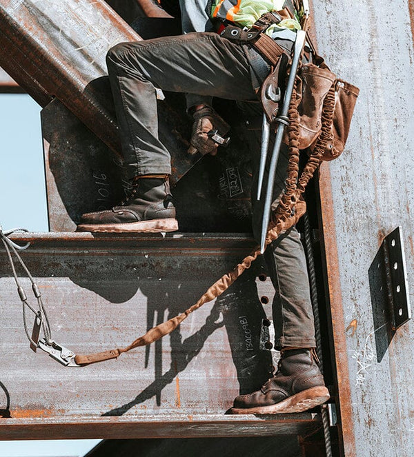 worker standing on edge of metal beam while wearing brown high top moccasin style boots with worn white soles