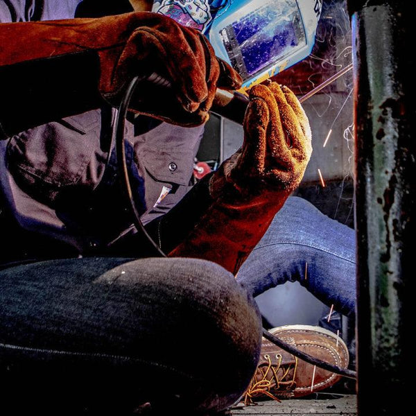 woman welding while wearing dark brown moccasin style boot with yellow and brown laces and white sole